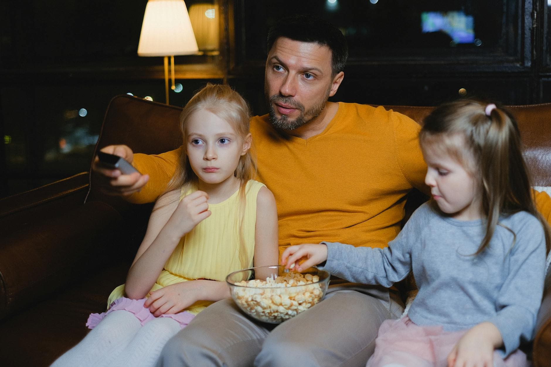 A father and his two daughters enjoying a movie night with popcorn on the couch.