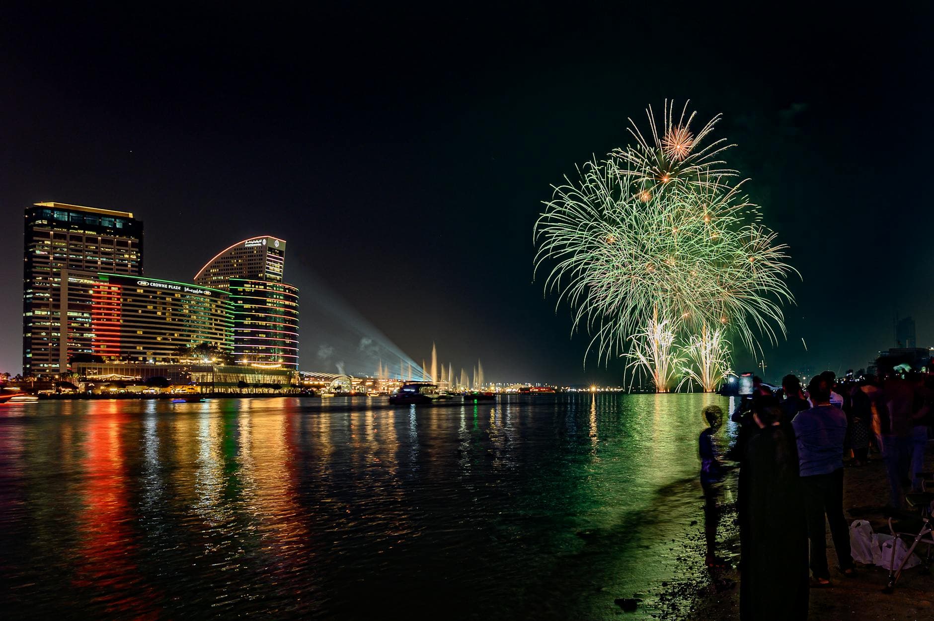 Colorful fireworks illuminate Dubai's skyline with reflections on the water.