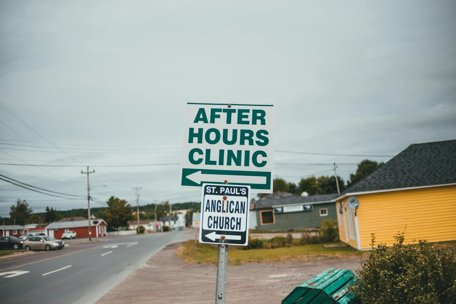 A pair of street signs directing to an after-hours clinic and St. Paul's Anglican Church on a suburban road.