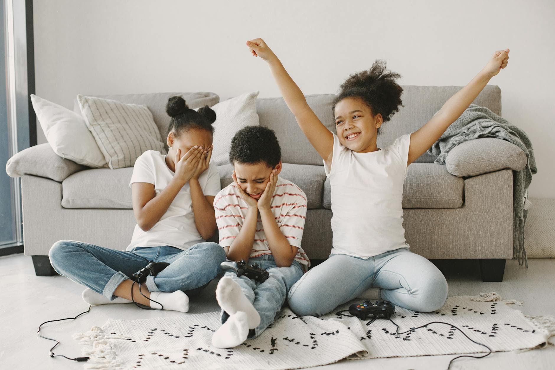 Three children sitting on the floor indoors playing video games with joy and expressions.