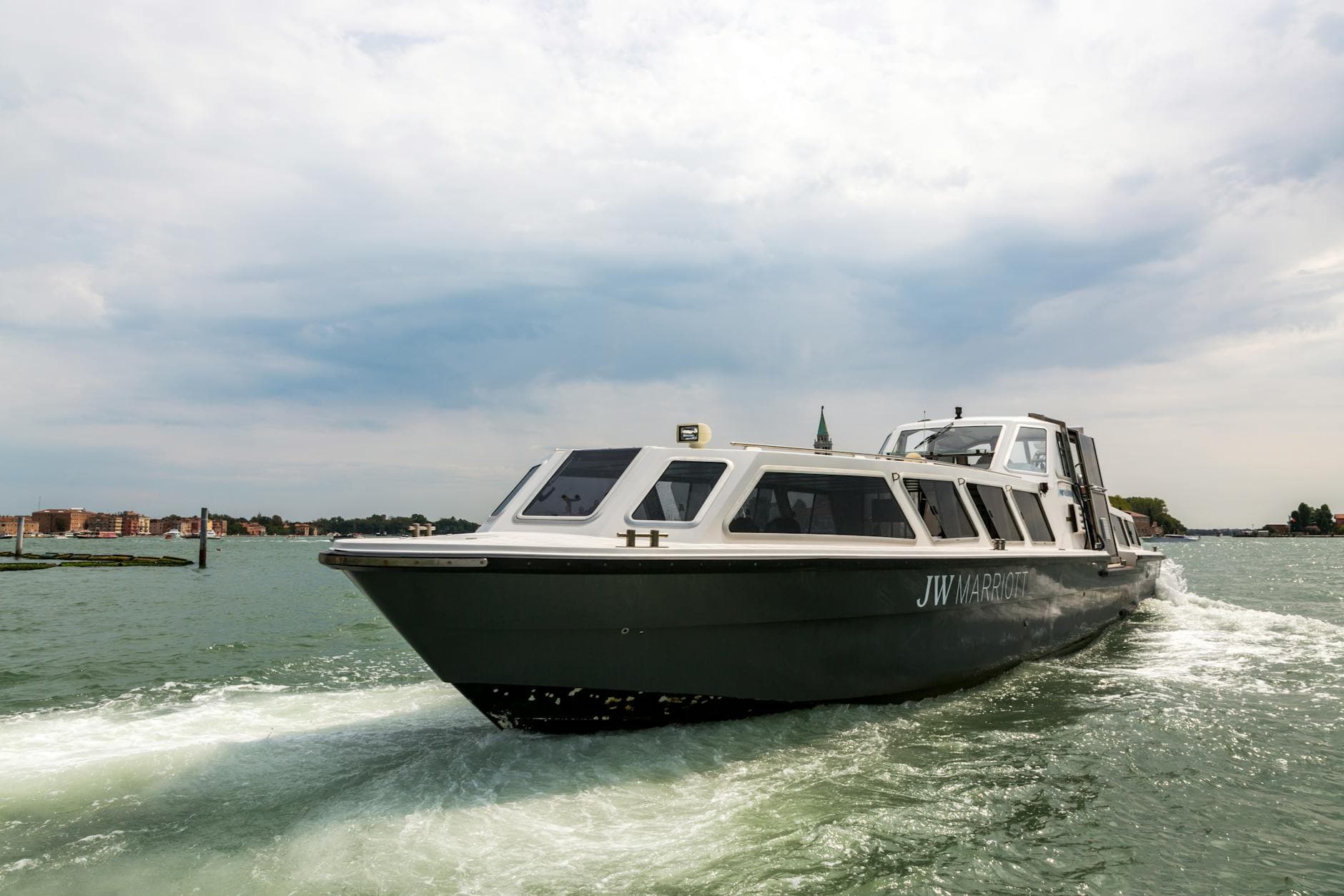 A sleek, modern boat cruising through the scenic Venice lagoon with cityscape in the background.