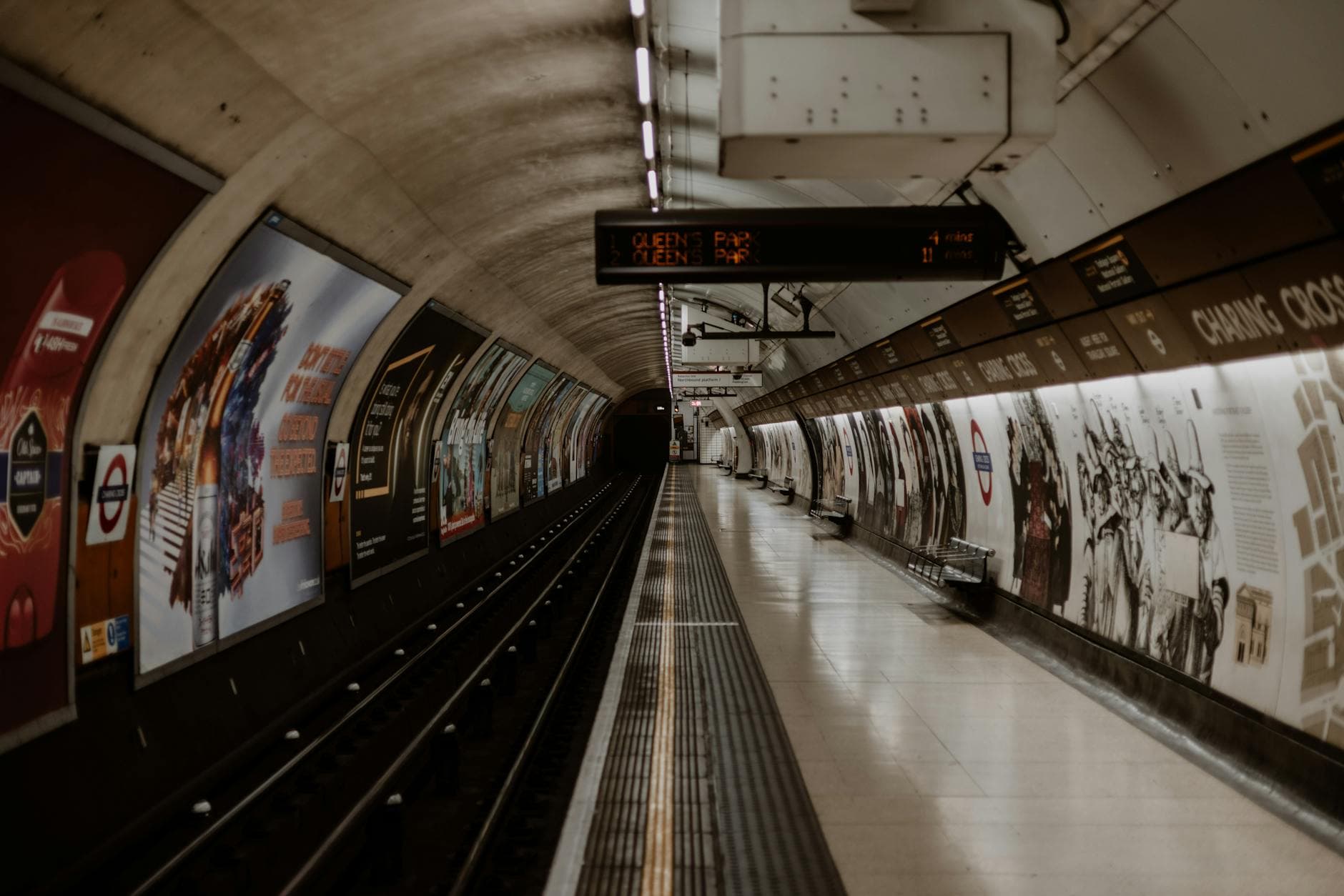Empty London Underground tube station platform with signs and advertisements.