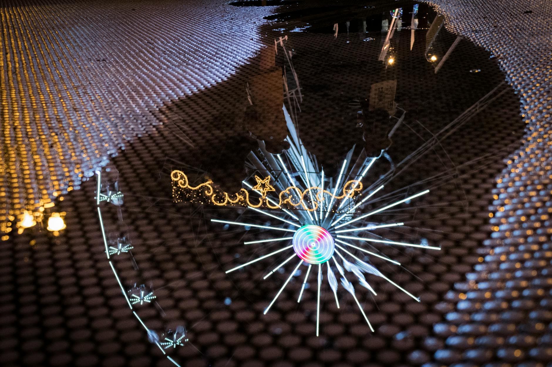 A vibrant reflection of Christmas lights and decorations captured in a wet puddle on a textured surface.