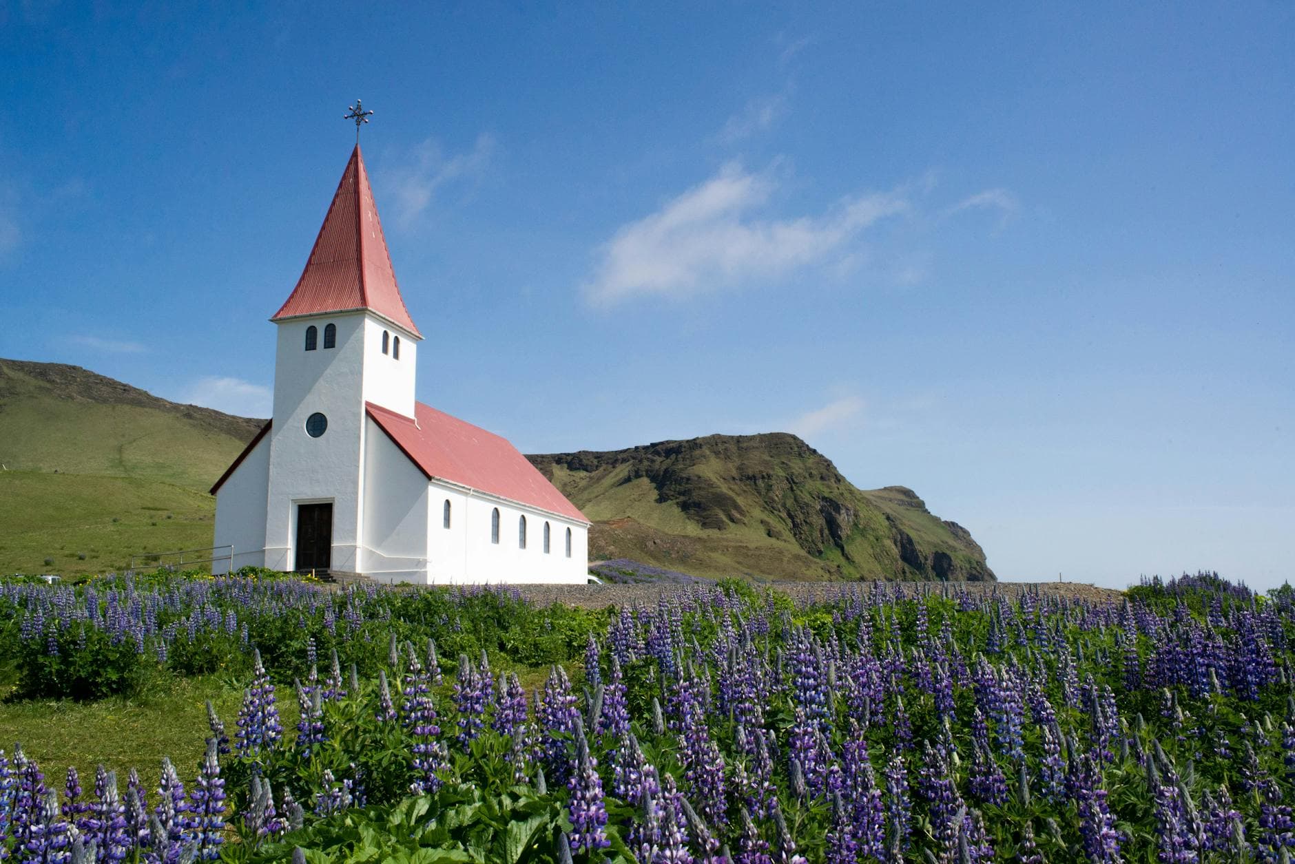 A picturesque view of Vik Church surrounded by blooming lavender fields with rolling hills in the background.