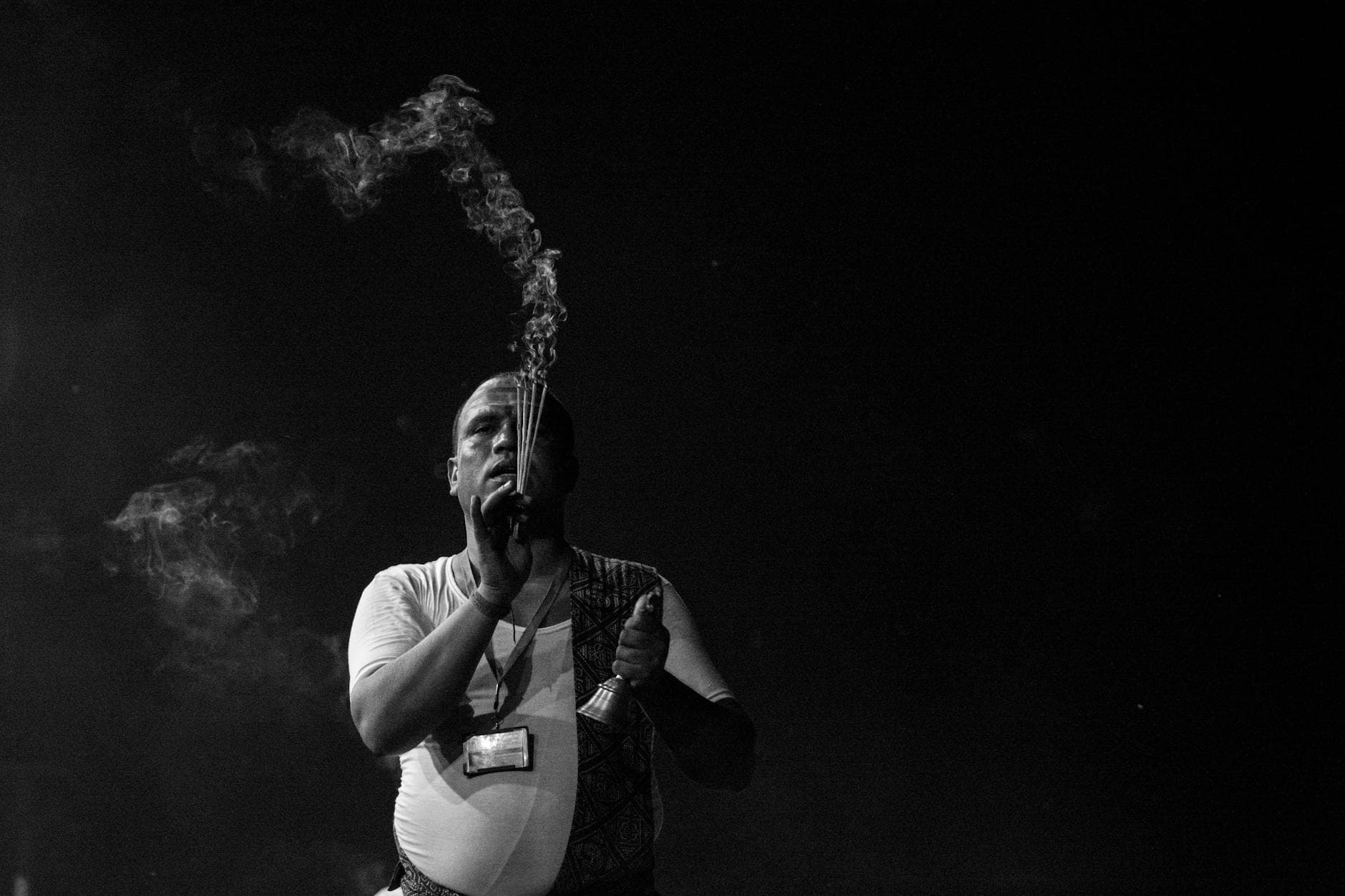 Black and white photo of a man performing a Hindu aarti with incense, creating serene smoke trails.