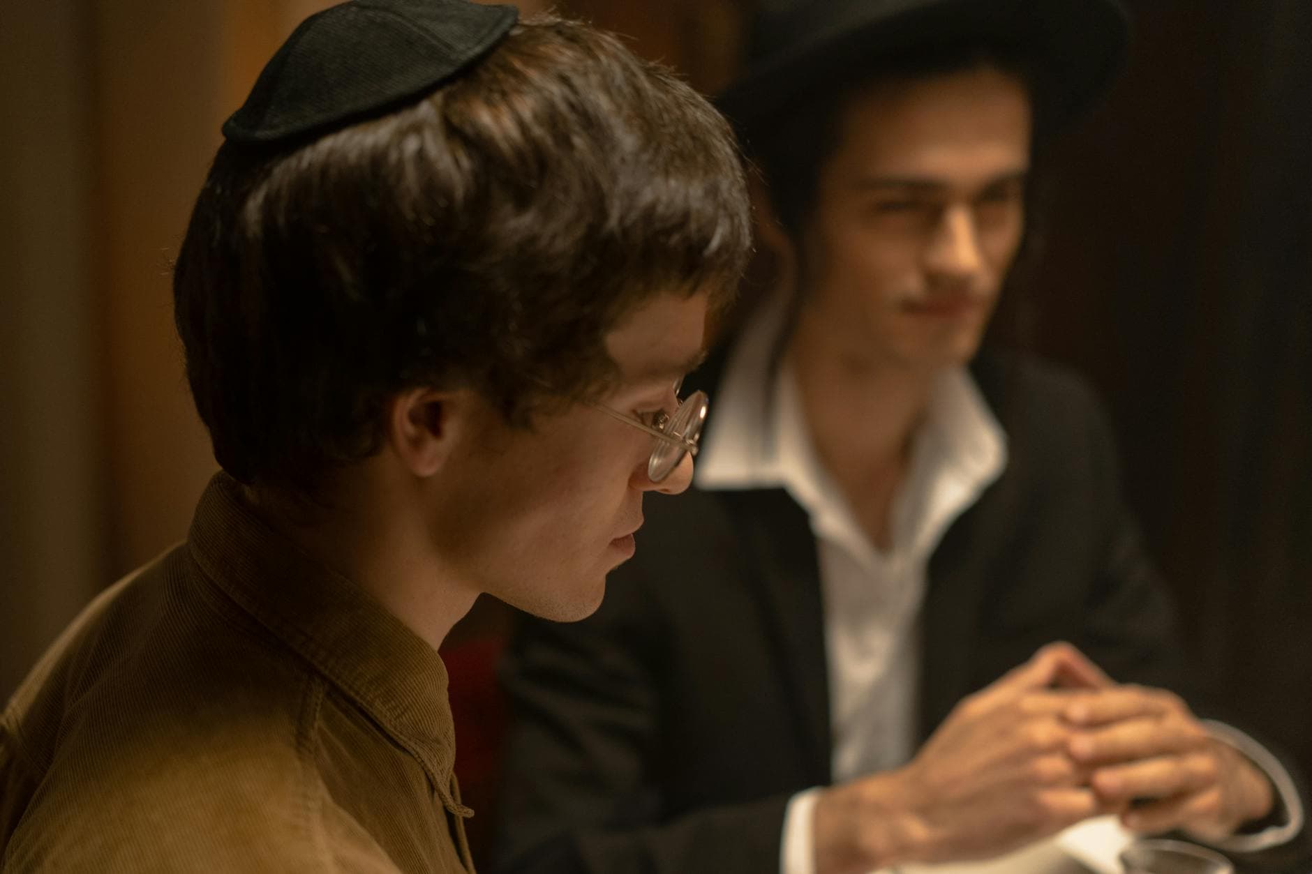 Two Jewish men in traditional attire having a serious conversation indoors.