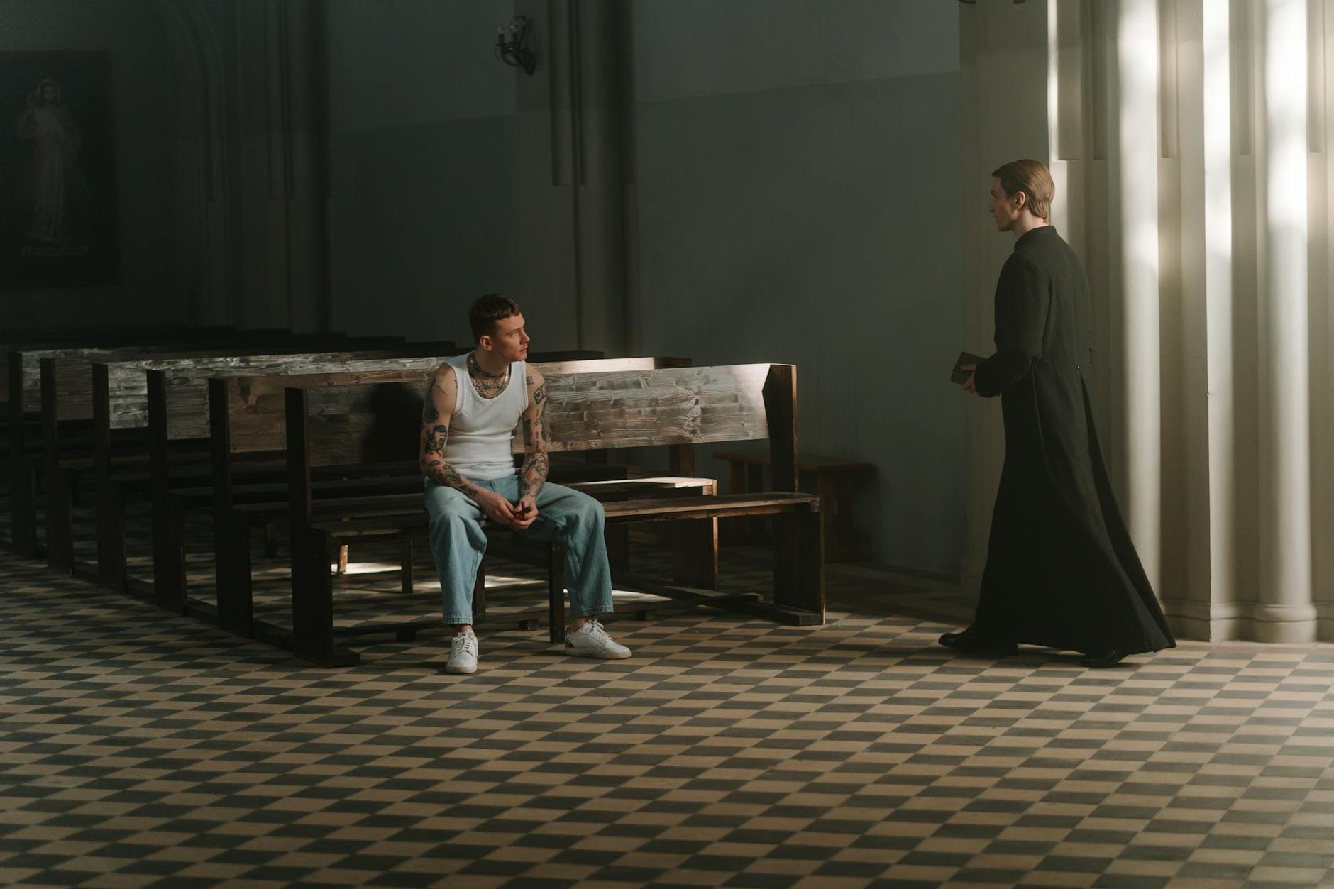 A tattooed man and a priest in a spiritual encounter within a church setting.
