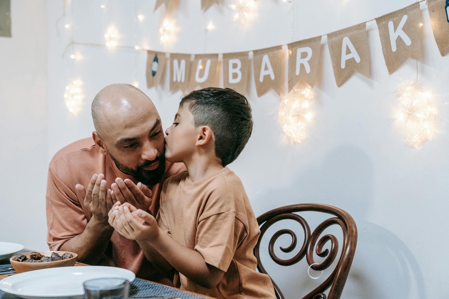 A touching moment between a father and son during an Eid Mubarak celebration indoors.