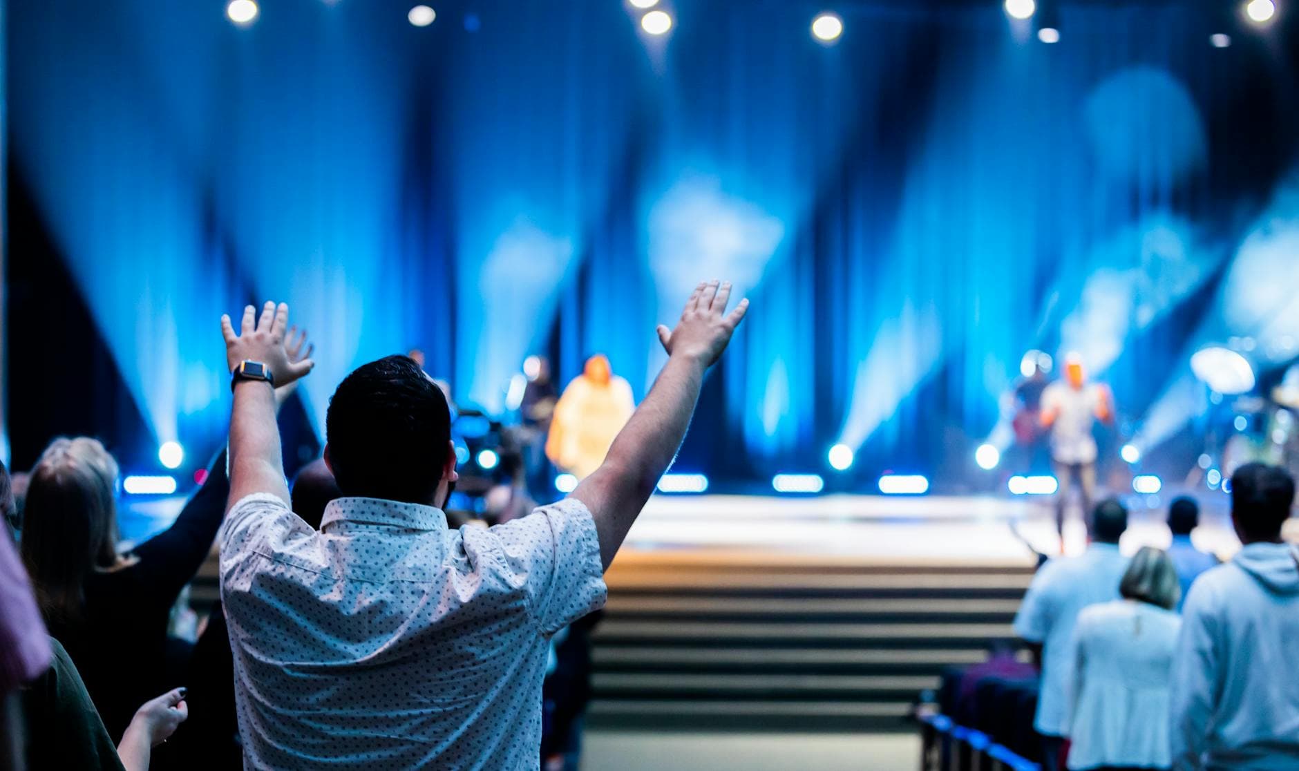 Group of people attending a lively worship service in a modern auditorium setting.