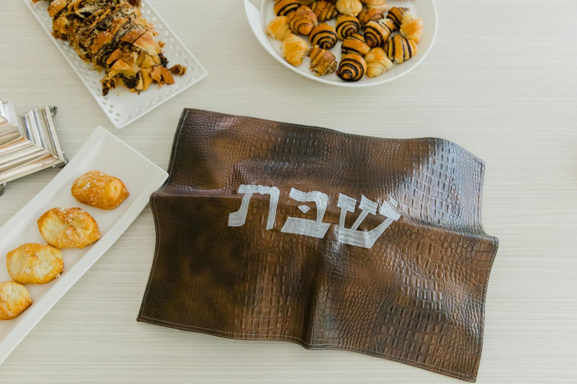 Top view of a Shabbat setup with challah, rugelach, and pastries on a table.