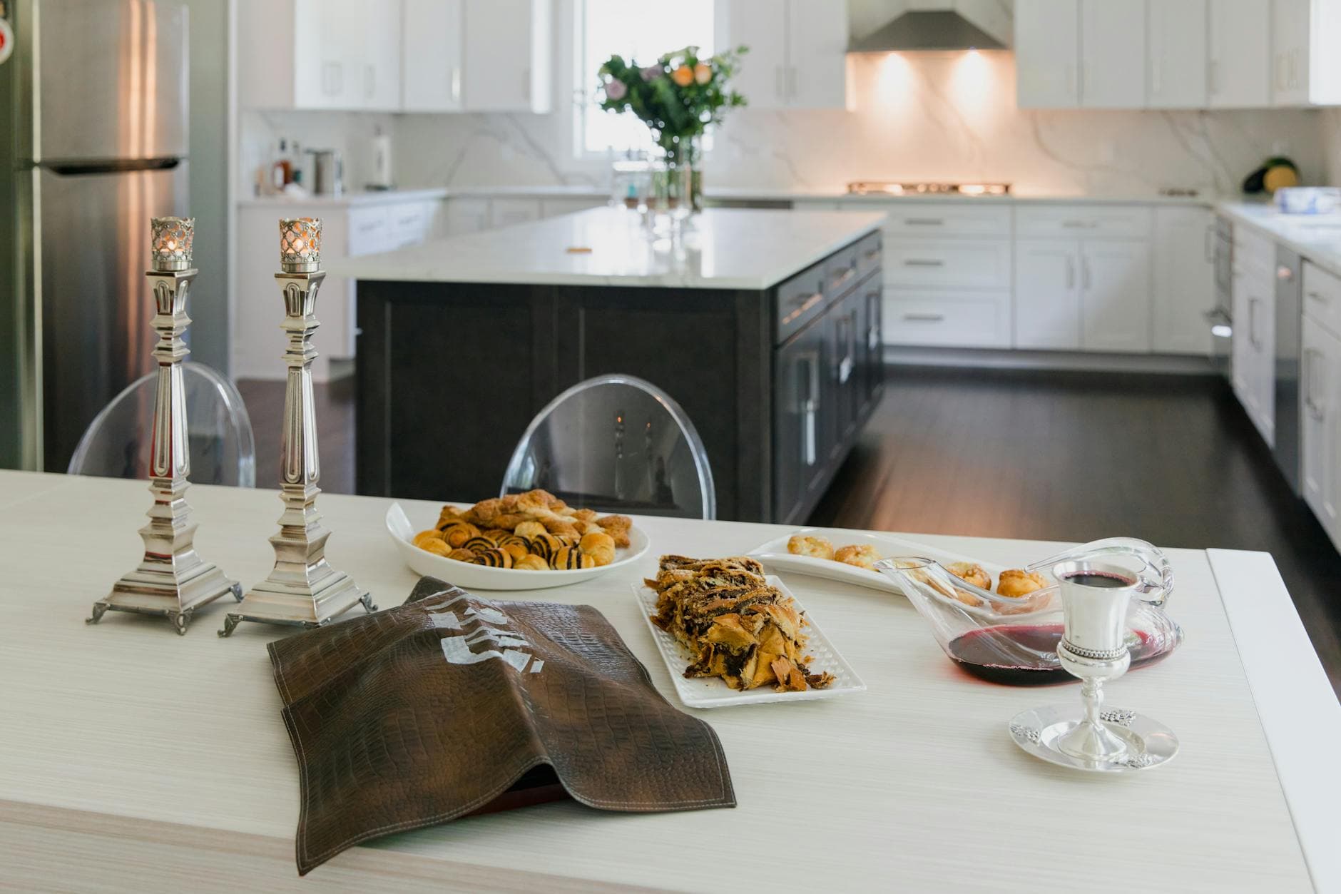 A modern kitchen setup featuring a Sabbath table with baked goods, candles, and wine.