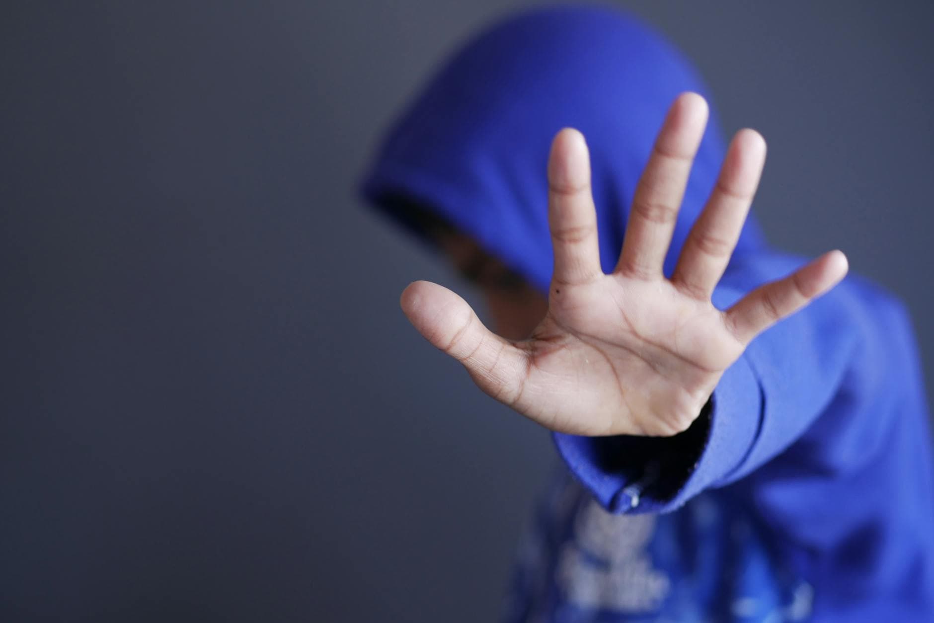 Close-up of a child in a blue hoodie holding up a hand. Blurred background and selective focus.