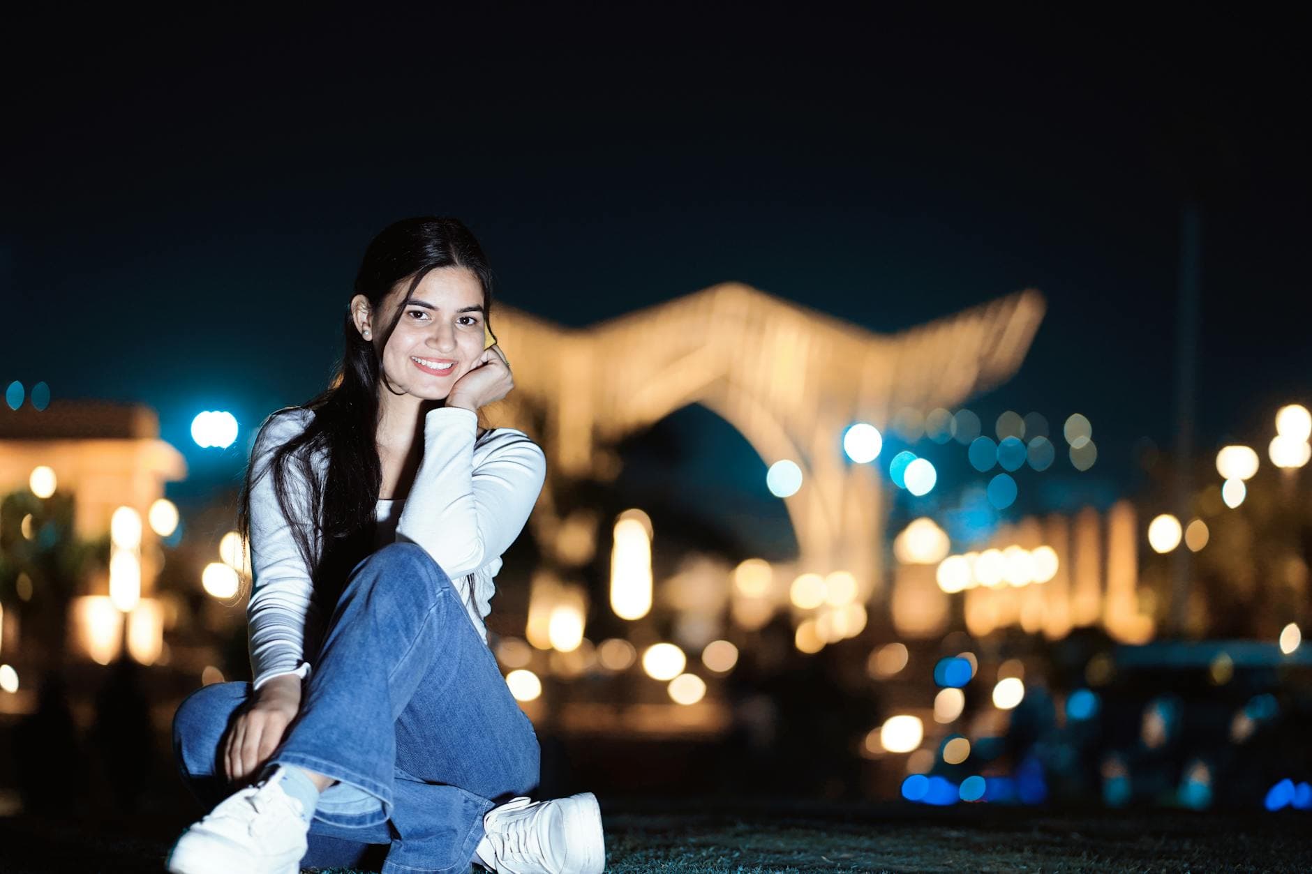 Portrait of a young woman smiling outdoors at night with city lights in the background.