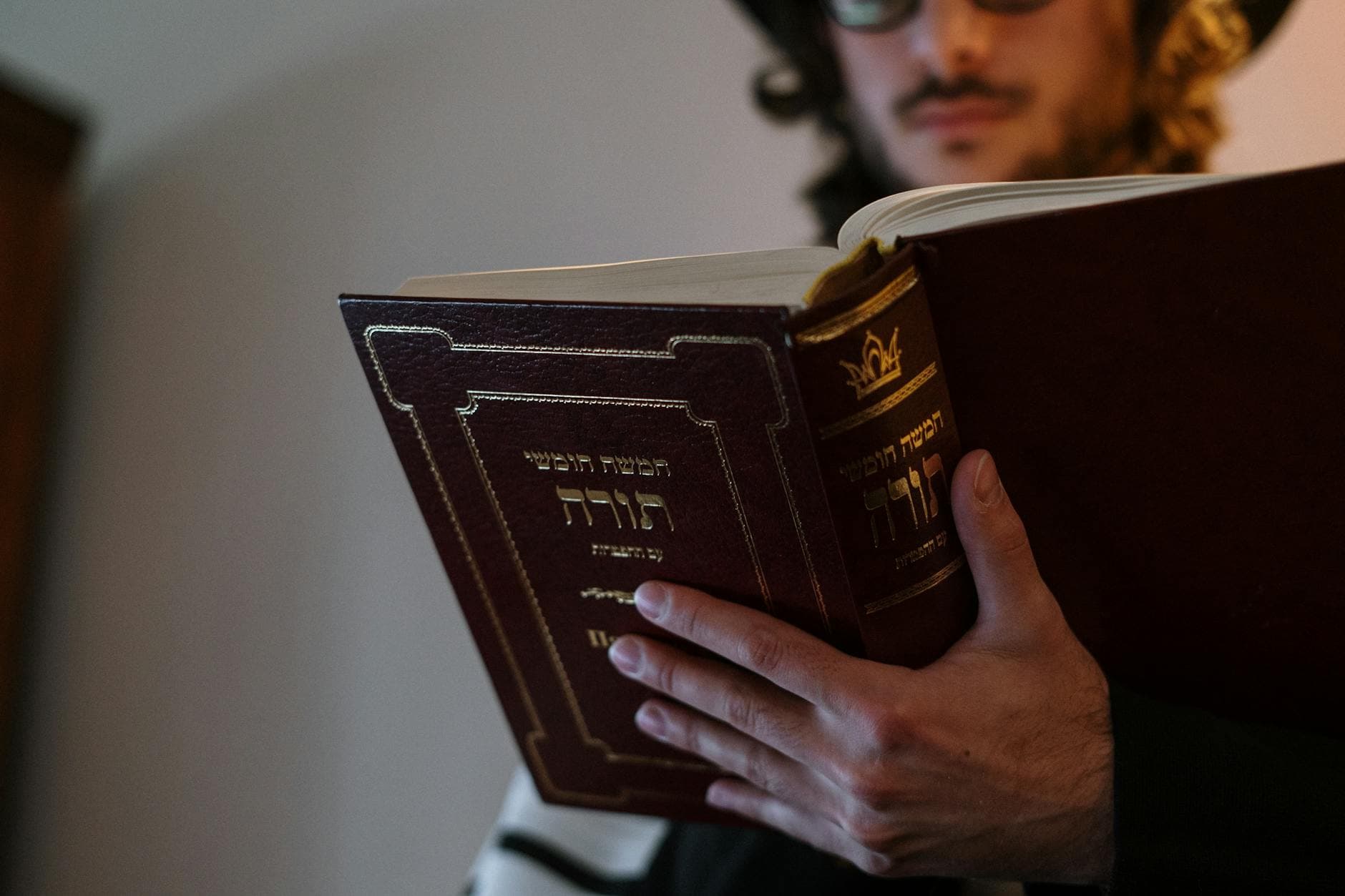 Orthodox Jewish man reading Torah with Hebrew text during Shabbat indoors, emphasizing tradition and culture.