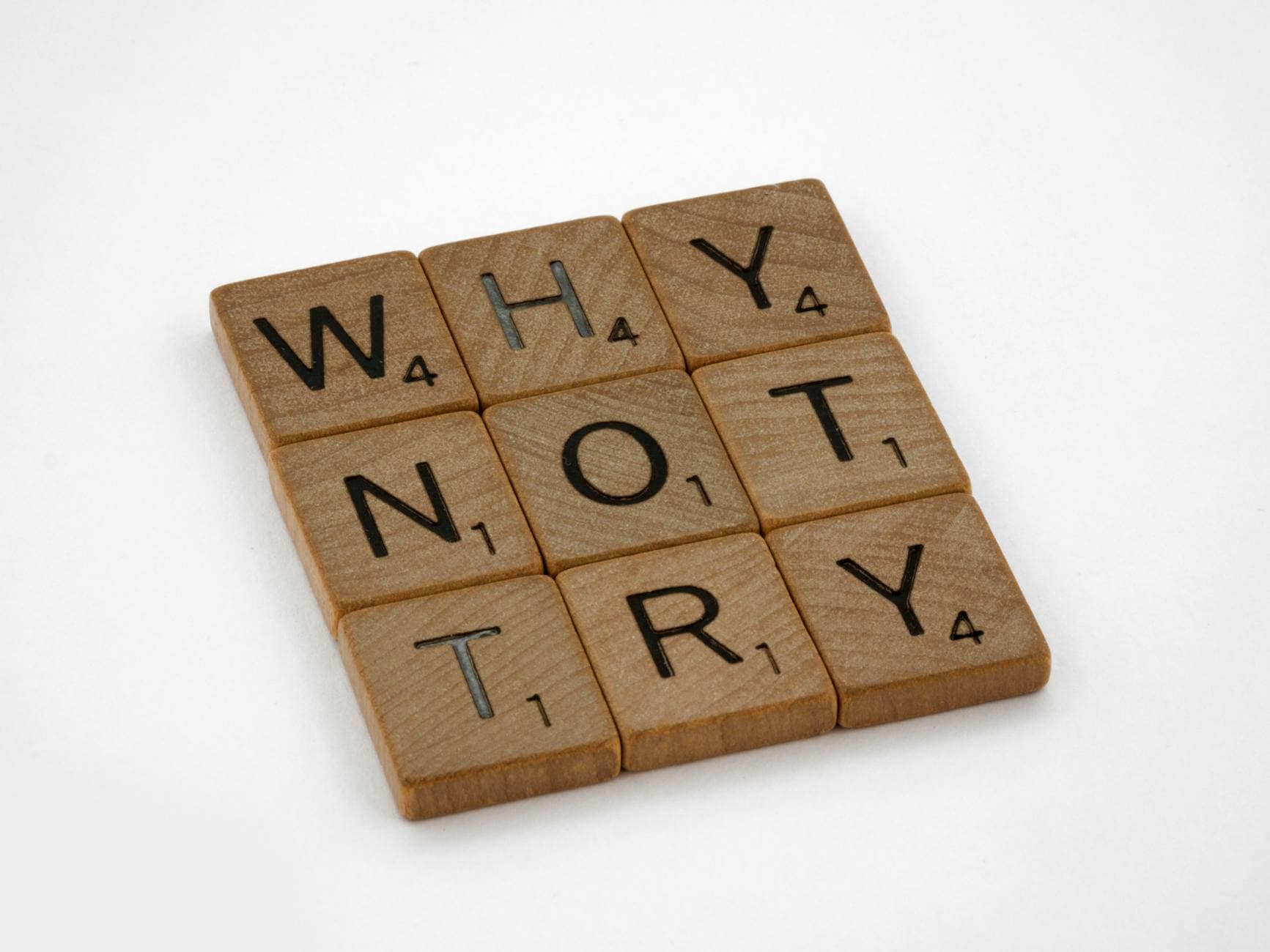 Wooden Scrabble tiles on a white background spelling the phrase 'Why Not Try'.
