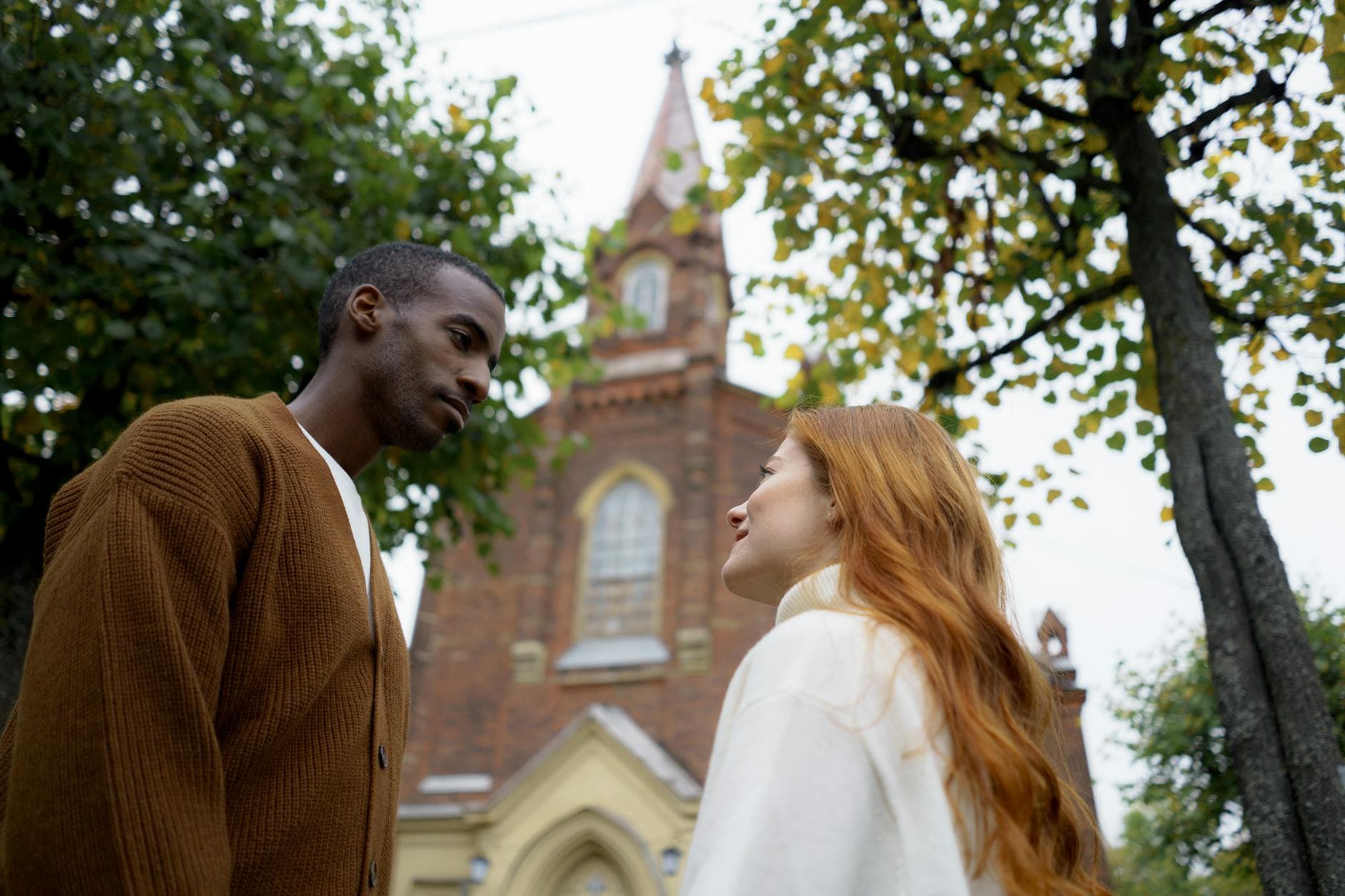 A couple shares a romantic moment outside a historical church in the autumn season.