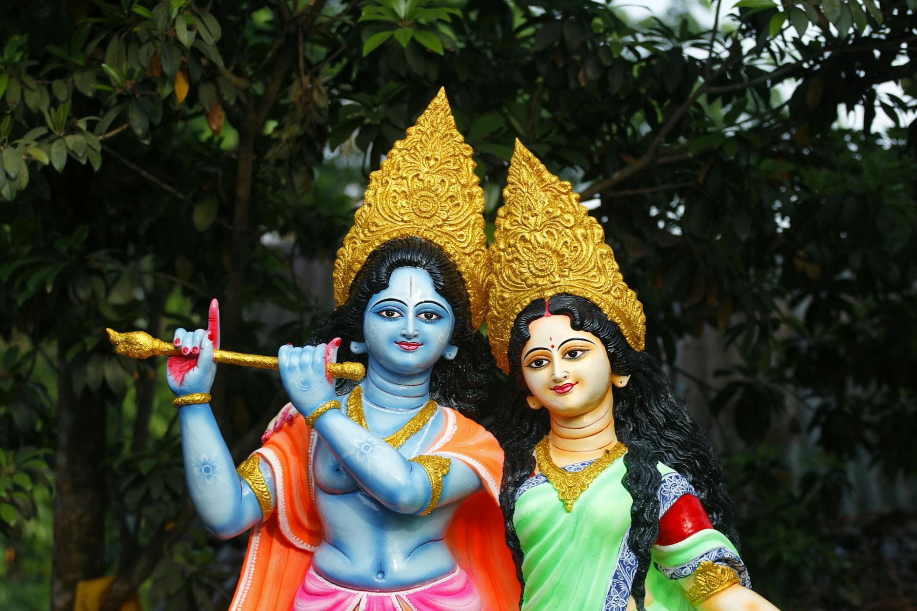 Vibrant sculptures of Krishna and Radha with intricate details set against a lush garden backdrop.