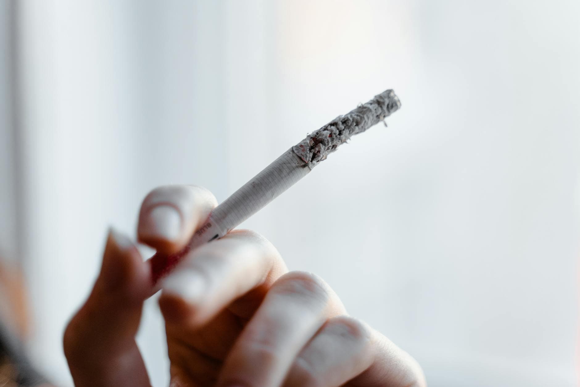 Detailed close-up of a hand holding a lit cigarette with ashes dropping.