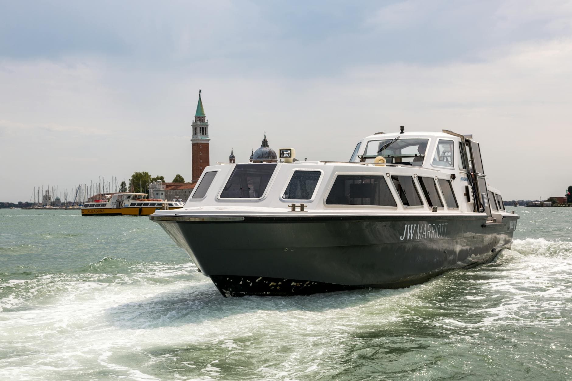 Water taxi cruising by San Giorgio Maggiore in Venice, Italy, under a cloudy sky.