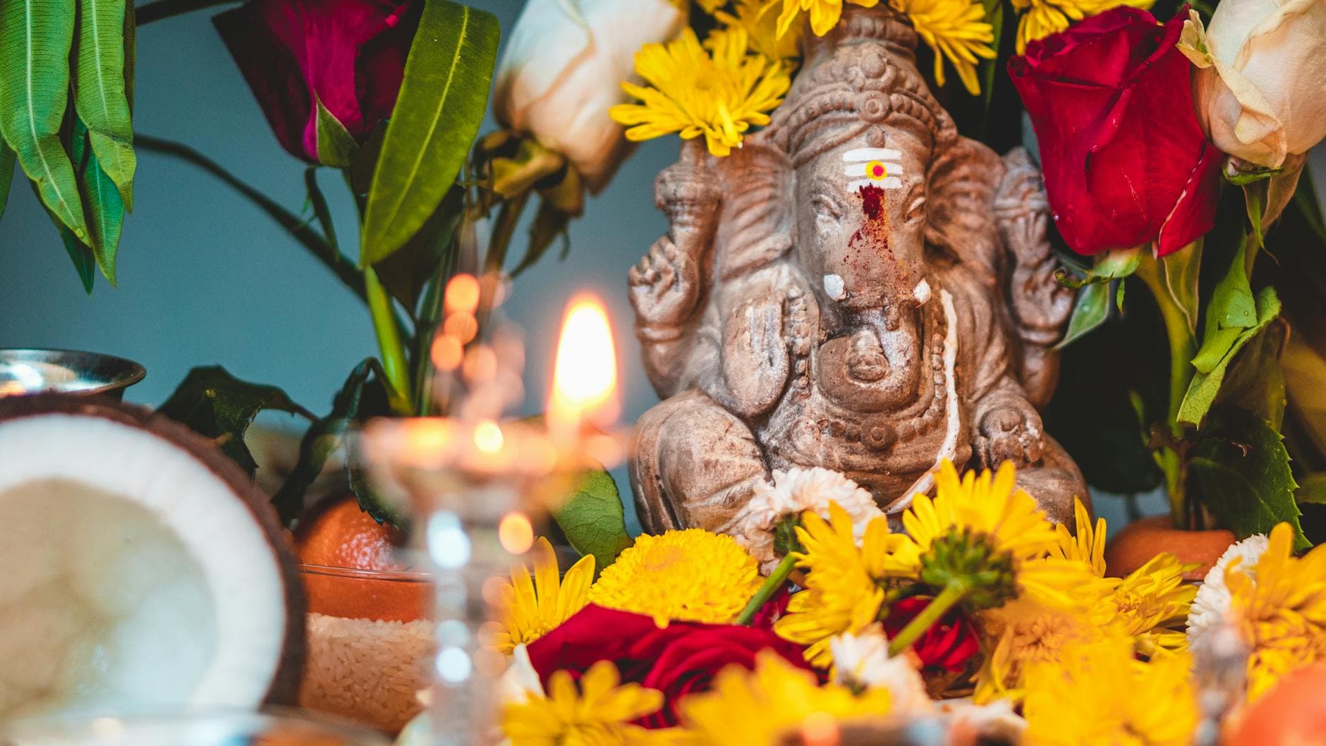 Close-up of a Ganesha statue adorned with vibrant flowers and a lit candle, creating a serene atmosphere.