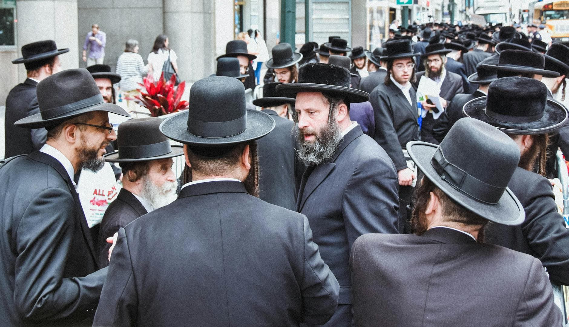 Group of Orthodox Jewish men gathered on a busy street in New York City.