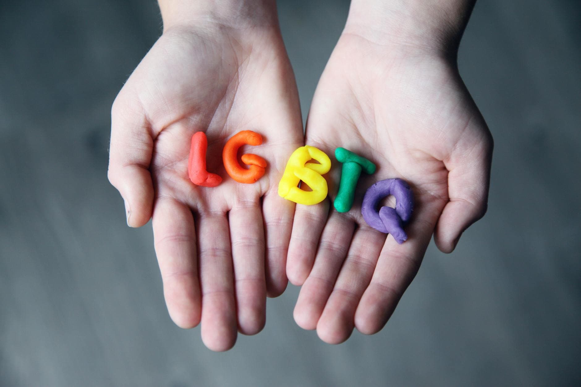 Close-up of hands holding colorful letters representing LGBTQ pride.