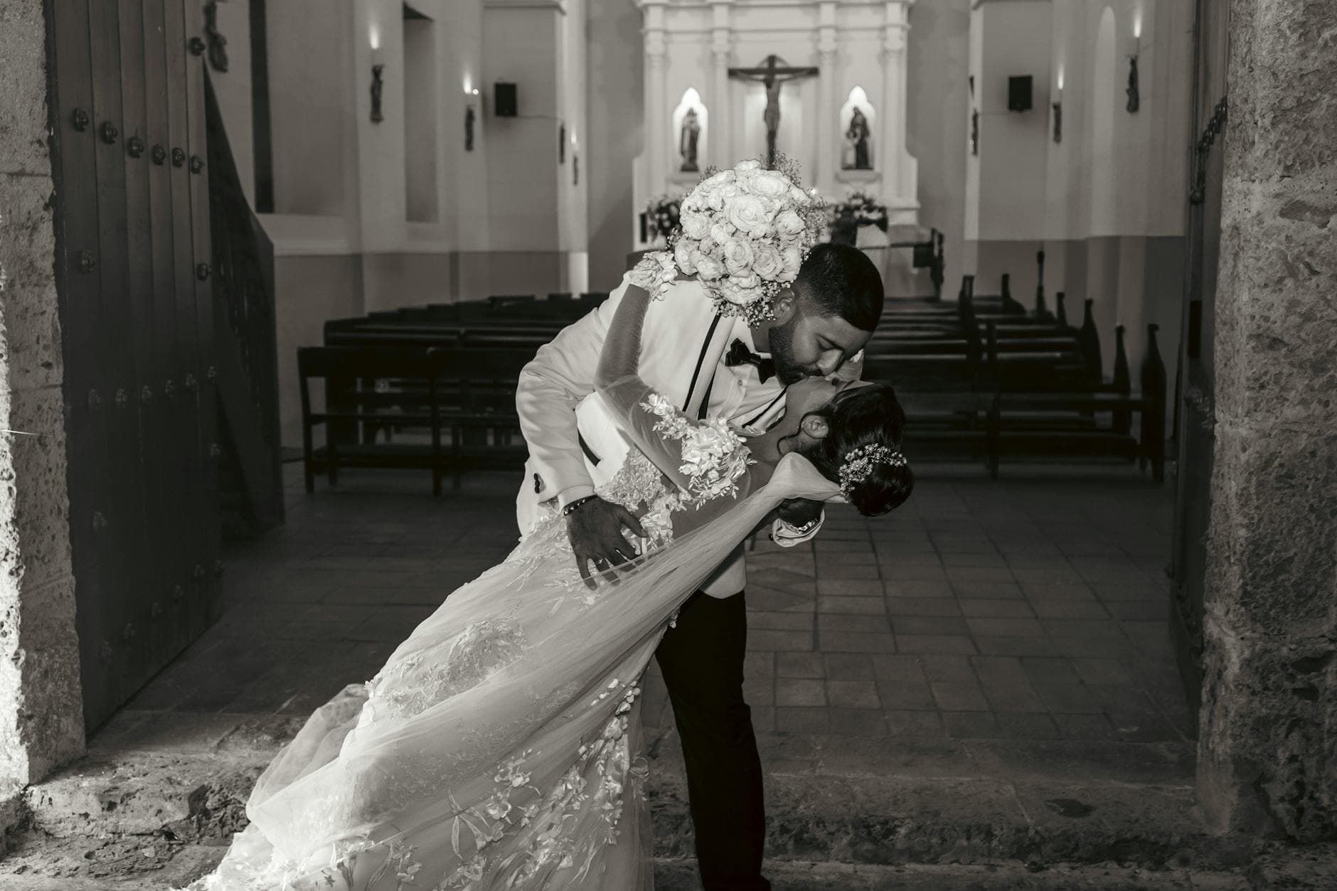 Bride and groom share a romantic kiss at their church wedding. Timeless love captured in black and white.