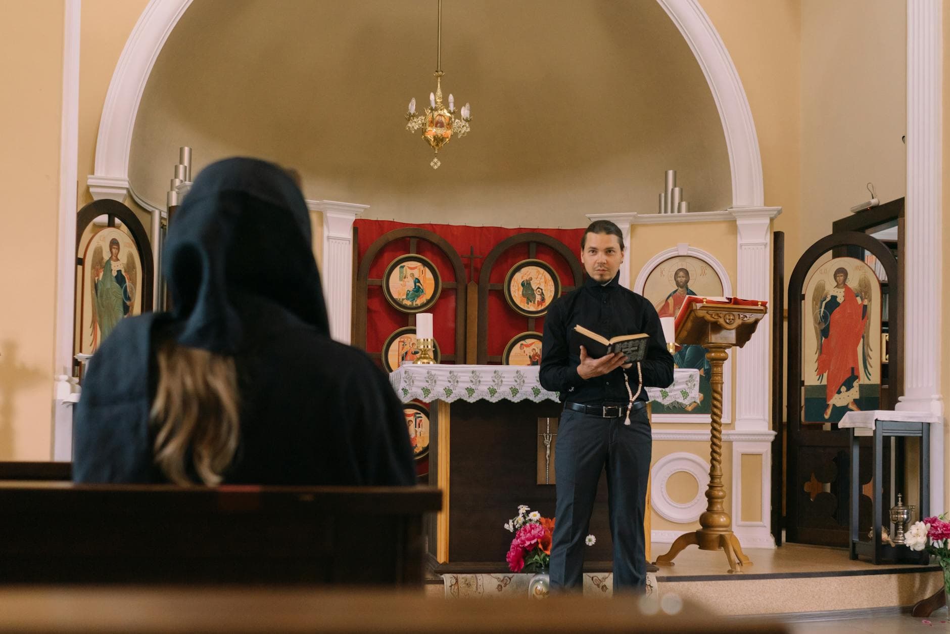 A priest reading scripture in a church with a person in the pews, emphasizing spirituality.